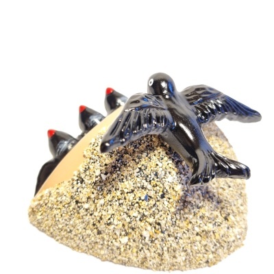 Escultura de aves pretas sobre base texturada que simula areia