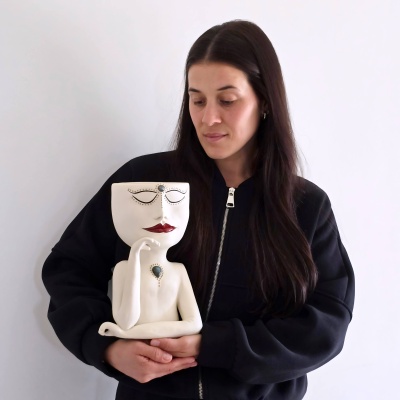Estatueta de cerâmica branca com rosto decorado e mulher a segurar