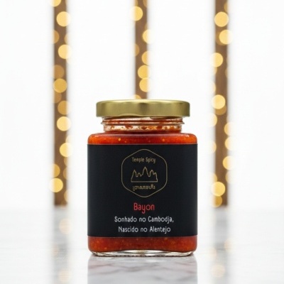 Frasco de molho ou pasta vermelha com rótulo preto sobre superfície branca e luzes de fundo amarelas desfocadas