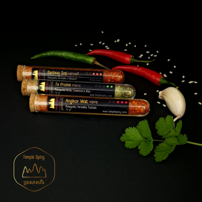 Três tubos de especiarias com rolha junto a pimentos, alho e folhas verdes sobre fundo escuro