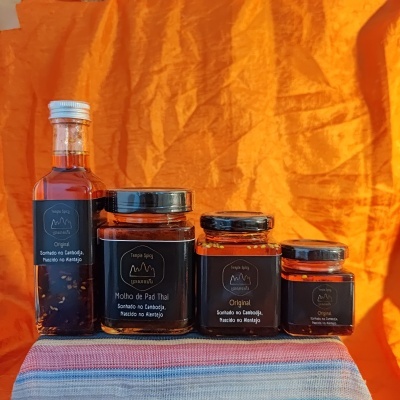 Frascos de molho Temple Spicy com etiquetas pretas, sobre tecido listrado, fundo laranja.