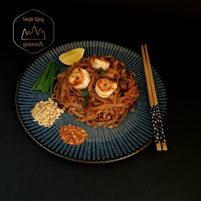 Prato com noodles, camarões, cebolinha, amendoins, pimenta e limão, com pauzinhos decorados.