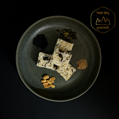 Quadrados de arroz crocante com várias sementes e amendoins num prato cinza escuro