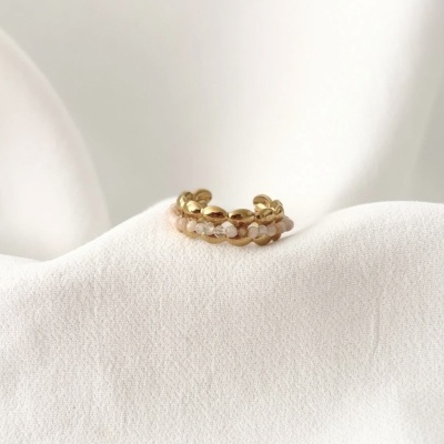 Anel dourado com pedras rosas e transparente sobre tecido branco.