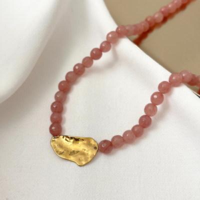 Colar com contas rosa e pendente dourado sobre tecido branco