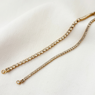 Dois braceletes dourados com pedras brilhantes sobre tecido branco