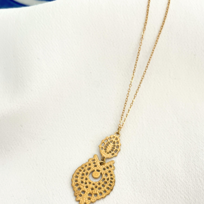 Colar dourado com pendente de folha rendado sobre tecido branco