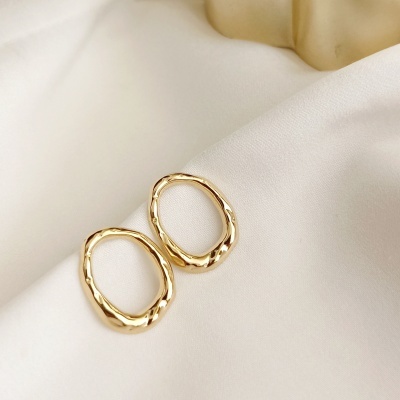 Par de brincos dourados ovais irregulares sobre tecido branco