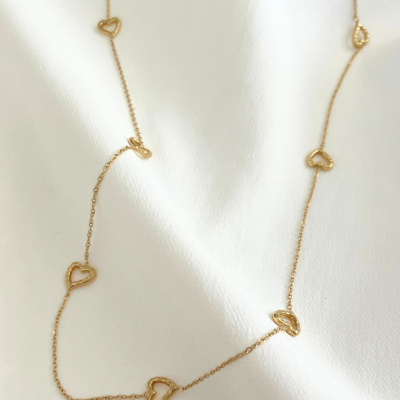 Colar dourado com corações em corrente fina sobre tecido branco.