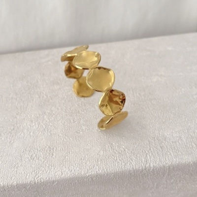 Anel dourado com elementos hexagonais martelados sobre superfície branca.