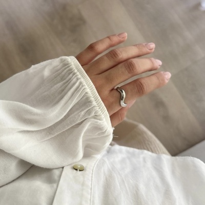Mão com anel prateado ondulado e camisa branca com botão