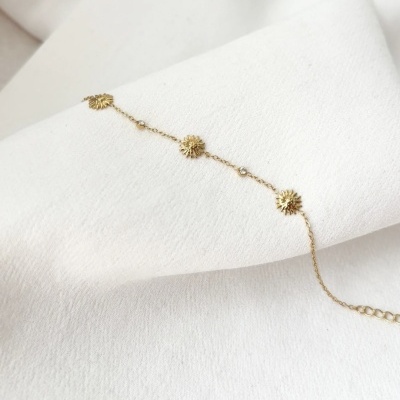 Pulseira dourada com pendentes de sol sobre tecido branco
