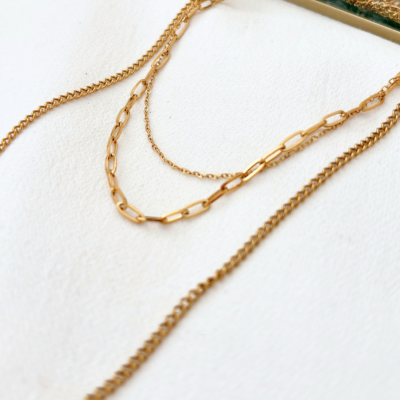 Três colares dourados com diferentes estilos de corrente em superfície branca