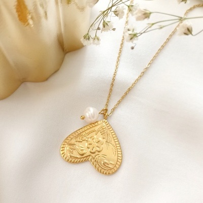 Colar dourado com coração e pérola sobre tecido branco