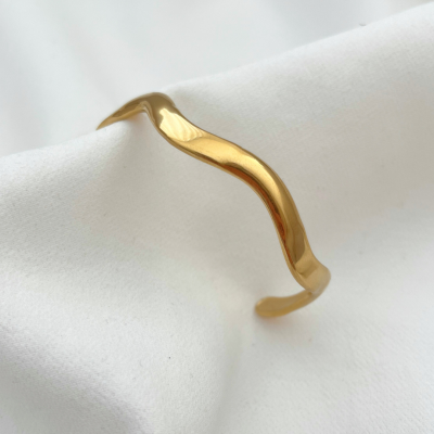 Pulseira dourada com design ondulado sobre tecido branco