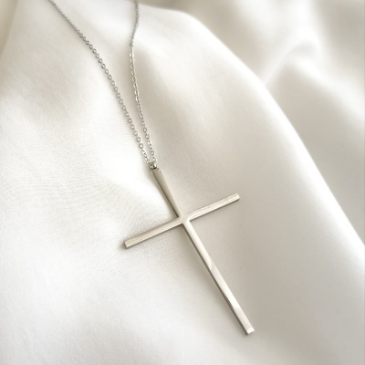 Colar prateado com pendente em forma de cruz sobre pano branco