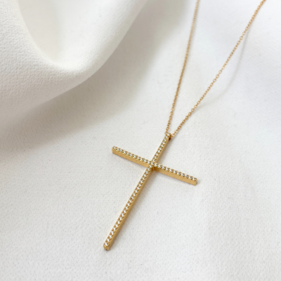 Colar com pendente em cruz dourada com pedras sobre tecido branco