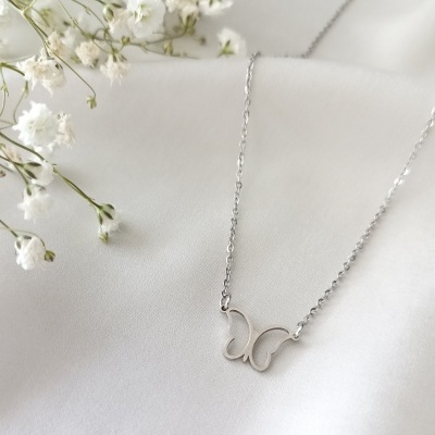 Colar prata com pendente de borboleta sobre tecido branco com flores brancas.