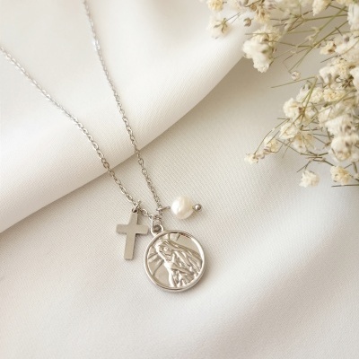Colar de prata com pingente redondo de figura feminina, cruz e pérola sobre tecido branco