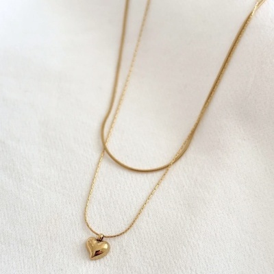 Colar dourado com pingente em forma de coração sobre tecido branco