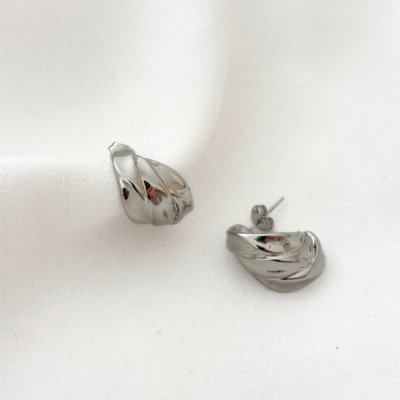 Brincos prateados com design torcido sobre tecido branco.