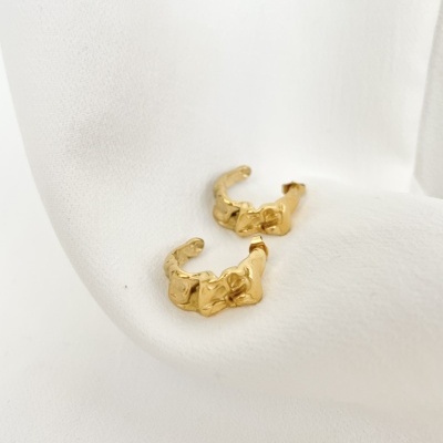 Brincos dourados com textura ondulada sobre tecido branco