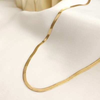 Colar dourado em corrente fina sobre tecido branco