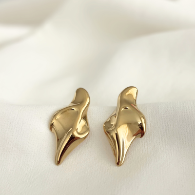 Brincos dourados em metal com design abstrato sobre tecido branco
