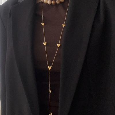 Gargantilha de contas e colar longo dourado com corações sobre roupa castanha e preta