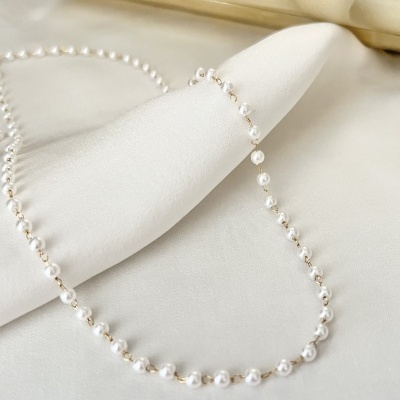 Colar de pérolas brancas com espaçadores prateados sobre tecido branco e bege