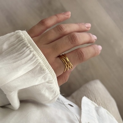 Mão com anel dourado de linhas entrelaçadas e camisa branca de tecido leve