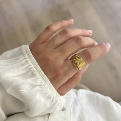 Mão usa dois anéis dourados e uma blusa branca com punho franzido