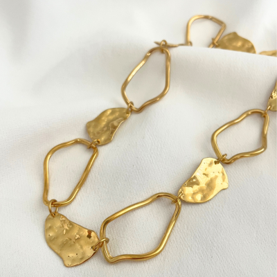 Colar dourado com elos irregulares sobre tecido branco