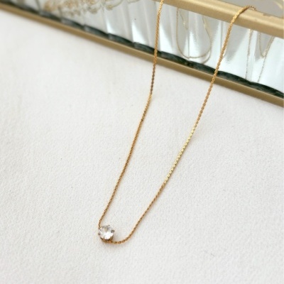 Colar dourado com pedra transparente, sobre superfície branca