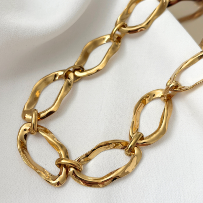 Colar com elos dourados irregulares sobre tecido branco