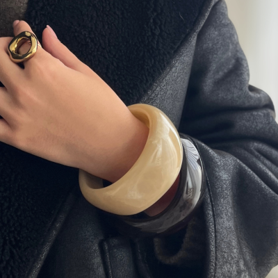 Braçadeiras bege e castanho com anel dourado em mão de mulher com casaco preto