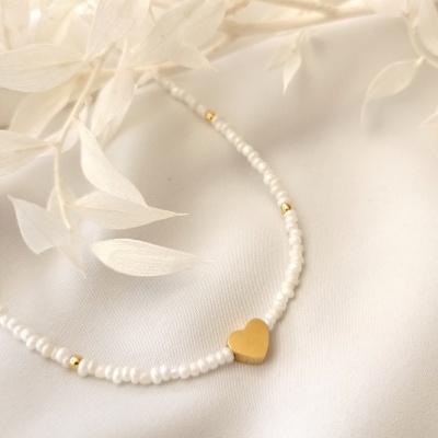 Colar de contas brancas e douradas com pendente de coração dourado sobre tecido branco