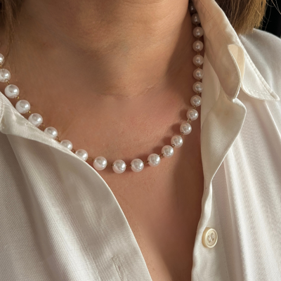 Colar de pérolas brancas redondas num pescoço com camisa branca