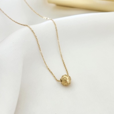 Colar dourado com pendente esférico e textura detalhada sobre tecido branco