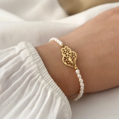 Pulseira com pérolas brancas e pendente dourado em pulso com camisa branca