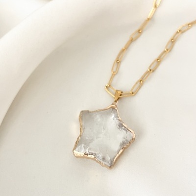 Colar dourado com pendente em estrela translúcida sobre tecido branco