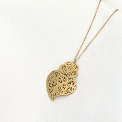 Colar dourado com pendente em forma de folhas sobre tecido branco