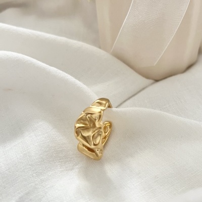 Anel dourado com textura ondulada sobre tecido branco