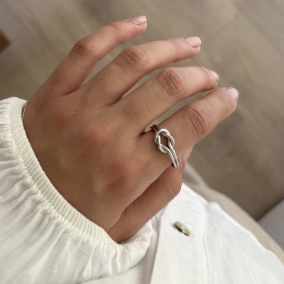 Mão com anel prateado entrelaçado e camisa branca