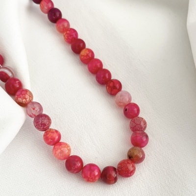 Colar de contas redondas em tons vermelhos e rosa sobre tecido branco
