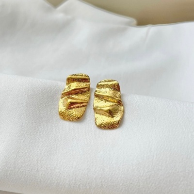 Brincos dourados texturizados sobre tecido branco