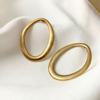 Brincos dourados ovalados sobre tecido branco