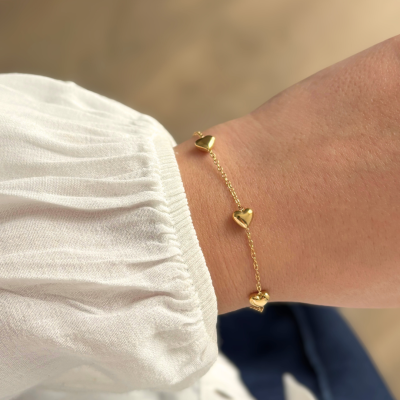 Pulseira dourada com corações no pulso de pessoa com camisa branca