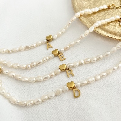 Pulseiras de pérolas com pingentes dourados em fundo branco e prato dourado.