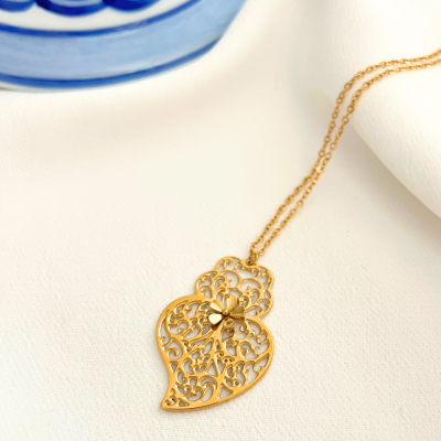 Colar dourado com pendente em forma de folha rendilhada sobre tecido branco